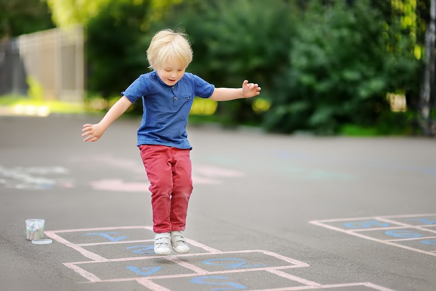 Child Playing Hopscotch On Playground Outdoors On A Sunny Day. A